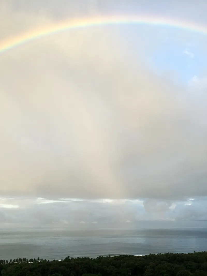 A faint rainbow over a cloudy sky and calm ocean.